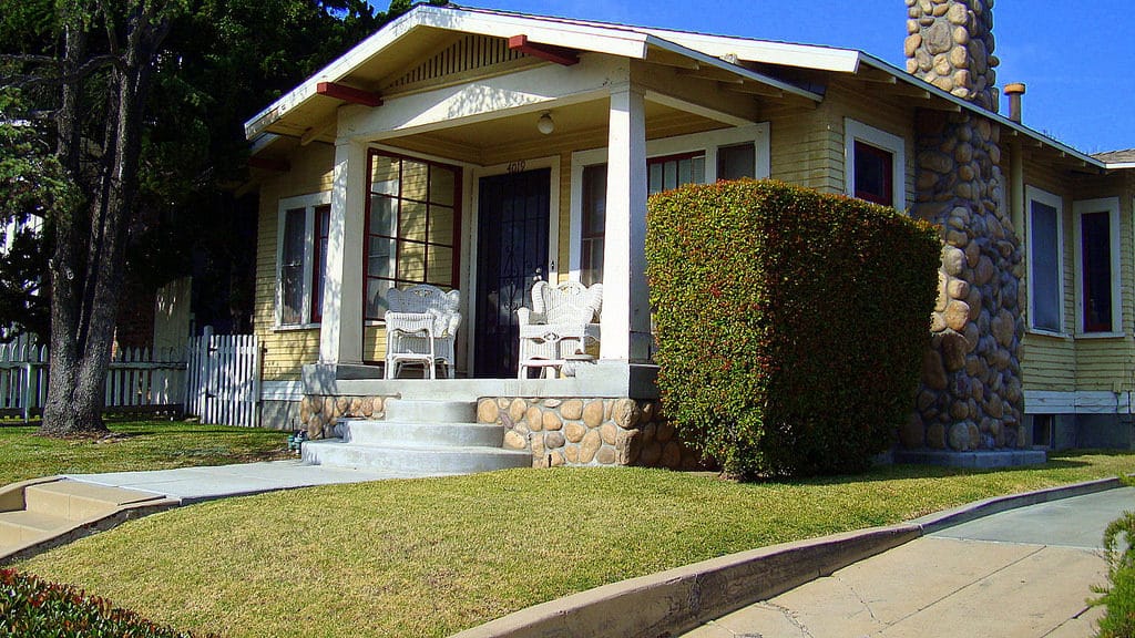 Cozy house with a porch and neatly trimmed hedge under a clear blue sky.