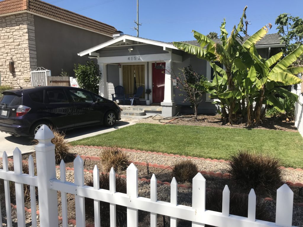 Small house with a green lawn and white picket fence under clear skies.