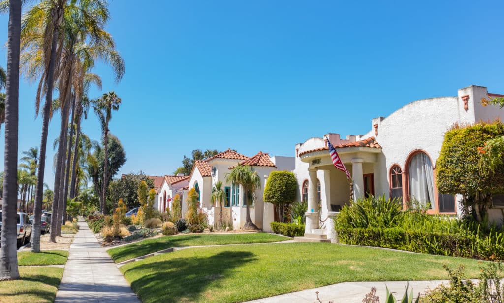 Sunny street with elegant, Mediterranean-style homes and well-kept lawns.